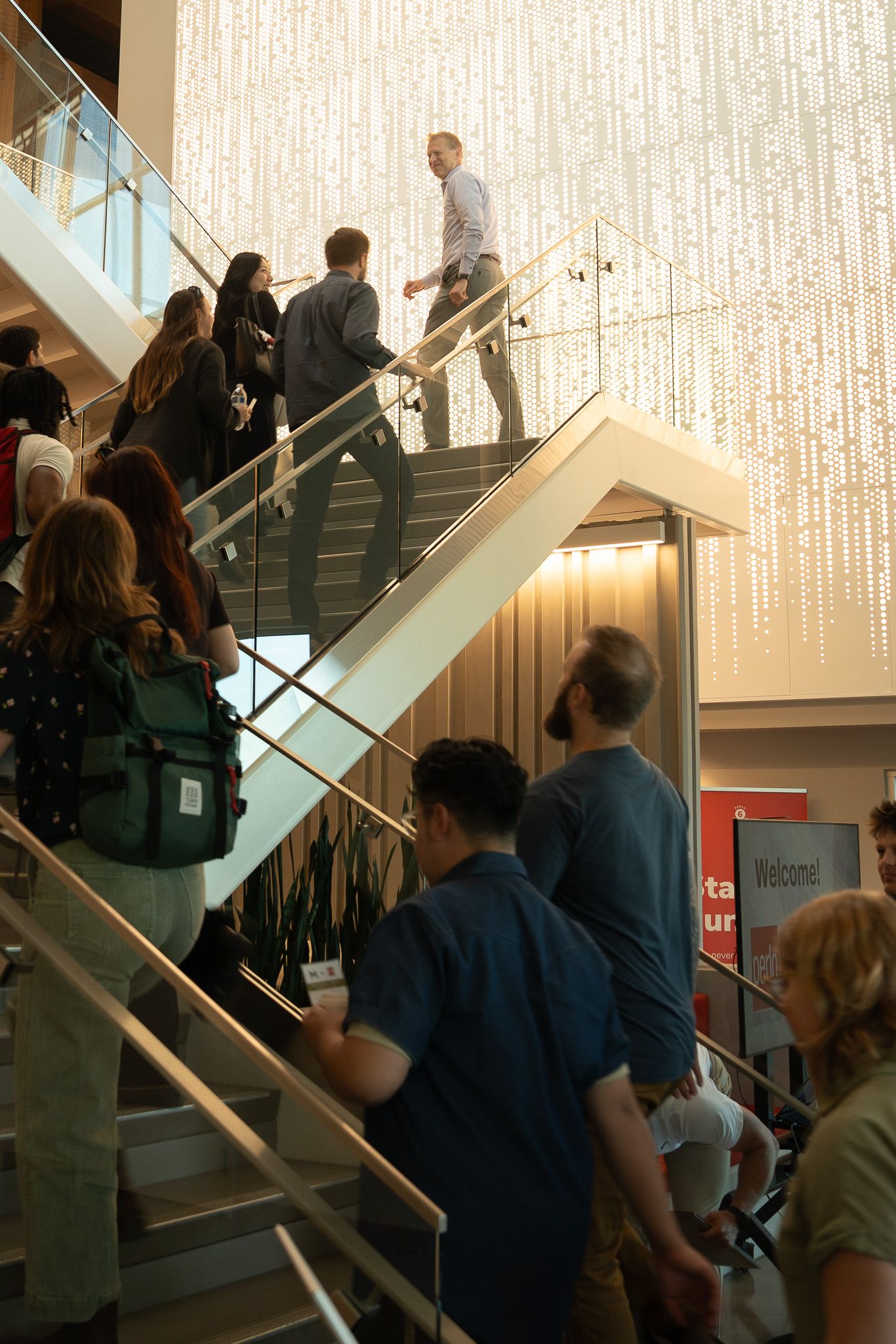 group of students completing internships at Mackenzie and Perlo ascend a staircase. A leader of Perlo stands at the front of the group. There's a bright light wall behind them